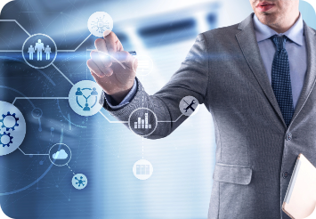 Businessman in a gray suit interacting with a digital interface, pointing at floating icons representing people, data charts, and technology, symbolizing connectivity and digital innovation in a corporate setting.